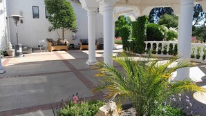 A covered outdoor area with white columns, seating, and potted plants.