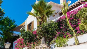 A white building with a sloped roof, surrounded by vibrant pink bougainvillea flowers and a palm tree. - Villa La Saliega Almuñécar by Ruralidays (Granada)