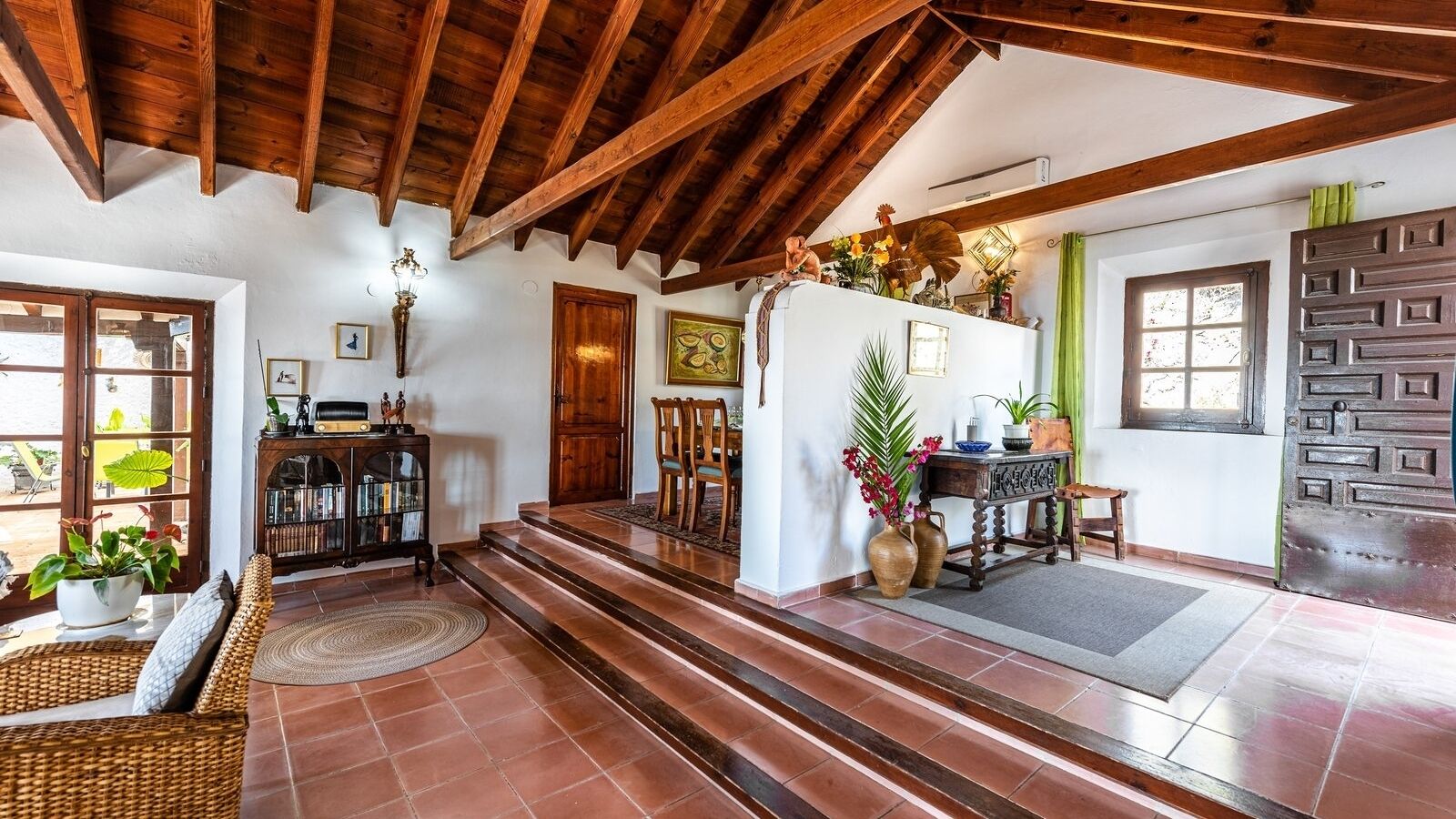 A spacious living area with a high ceiling, wooden beams, a fireplace, and a dining area with chairs and a table.
