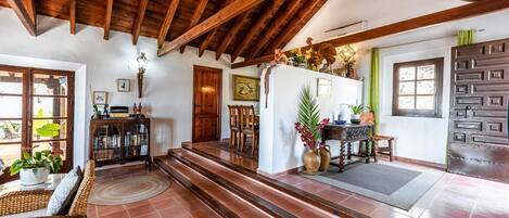 A spacious living area with a high ceiling, wooden beams, a fireplace, and a dining area with chairs and a table.