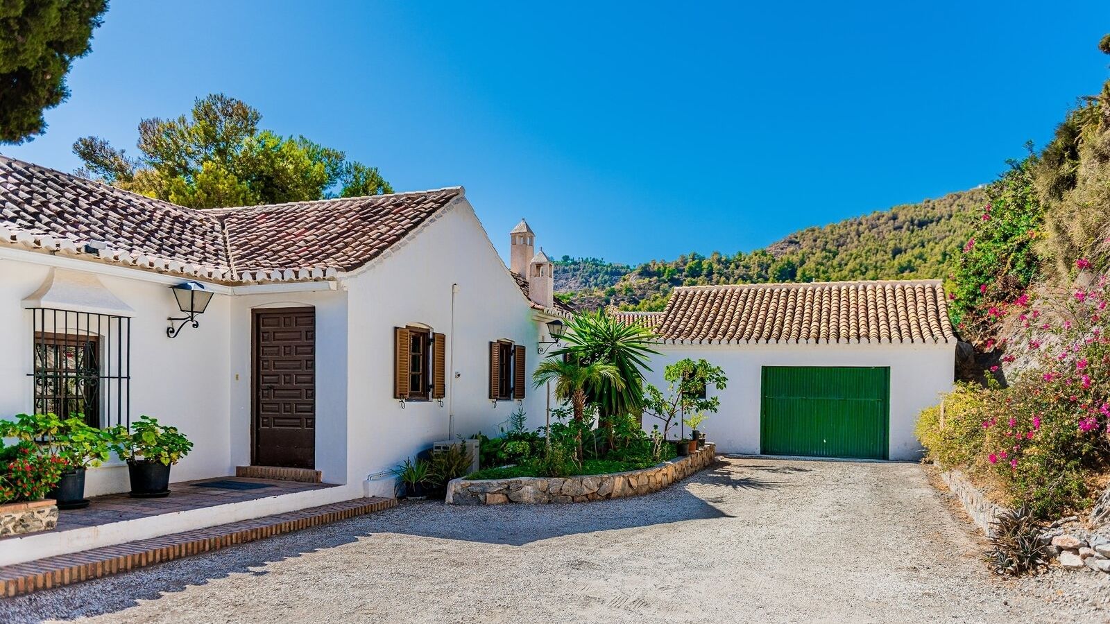 A white building with a tiled roof, a green door, and a gravel driveway.