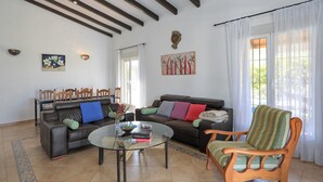 A living room with a sofa, armchair, and coffee table, a dining table with chairs, and a painting on the wall.