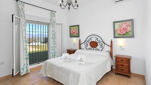 A bedroom with a bed, a nightstand, a dresser, a chandelier, and two framed pictures on the wall.