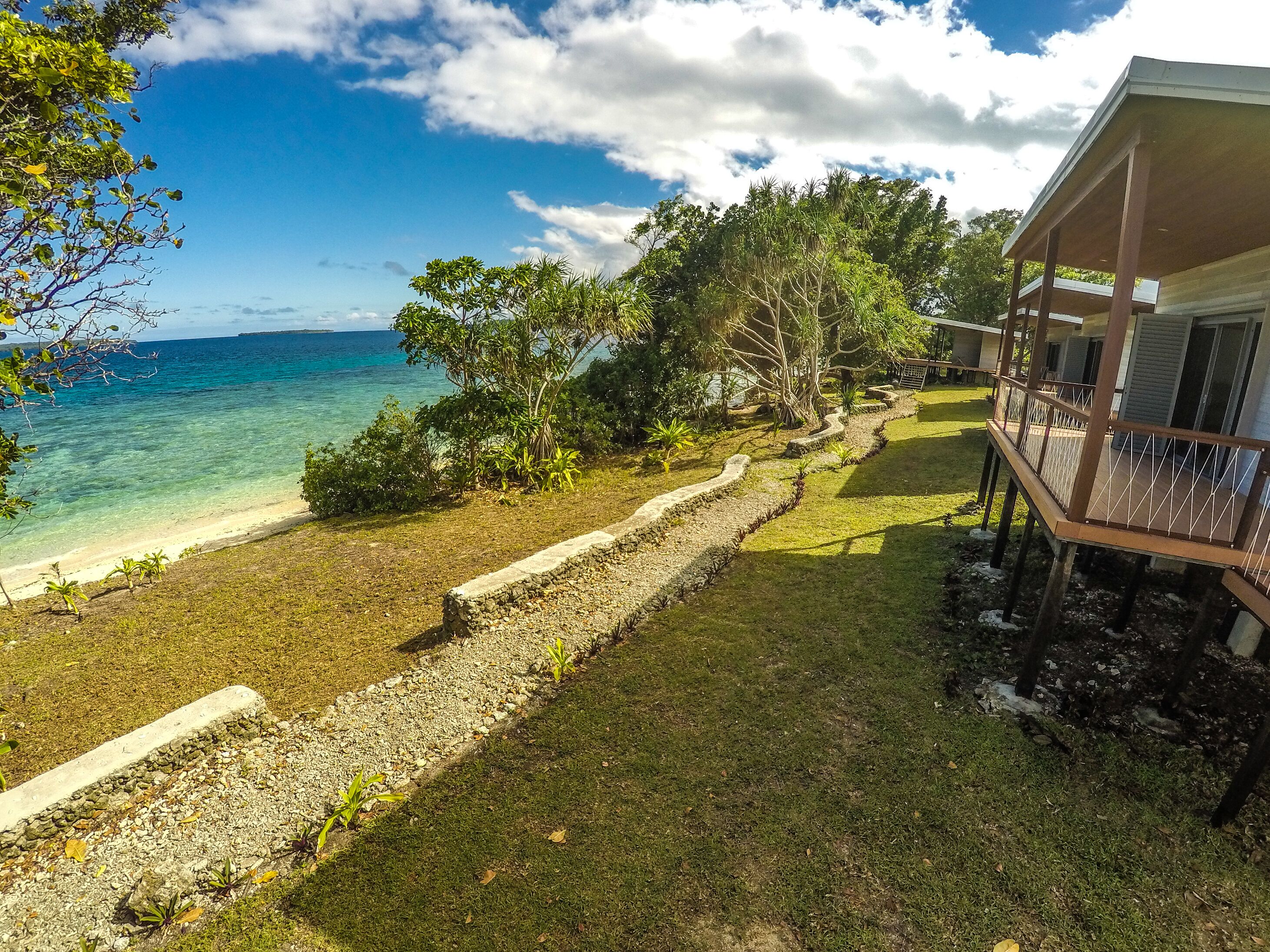A beachfront property with a grassy area, a pathway, and a wooden deck overlooking the ocean.