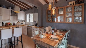 A rustic kitchen with a wooden dining table set for a meal, a built-in oven, and a large cabinet with glass doors. - Casa Siempre Sayalonga by Ruralidays (Málaga)