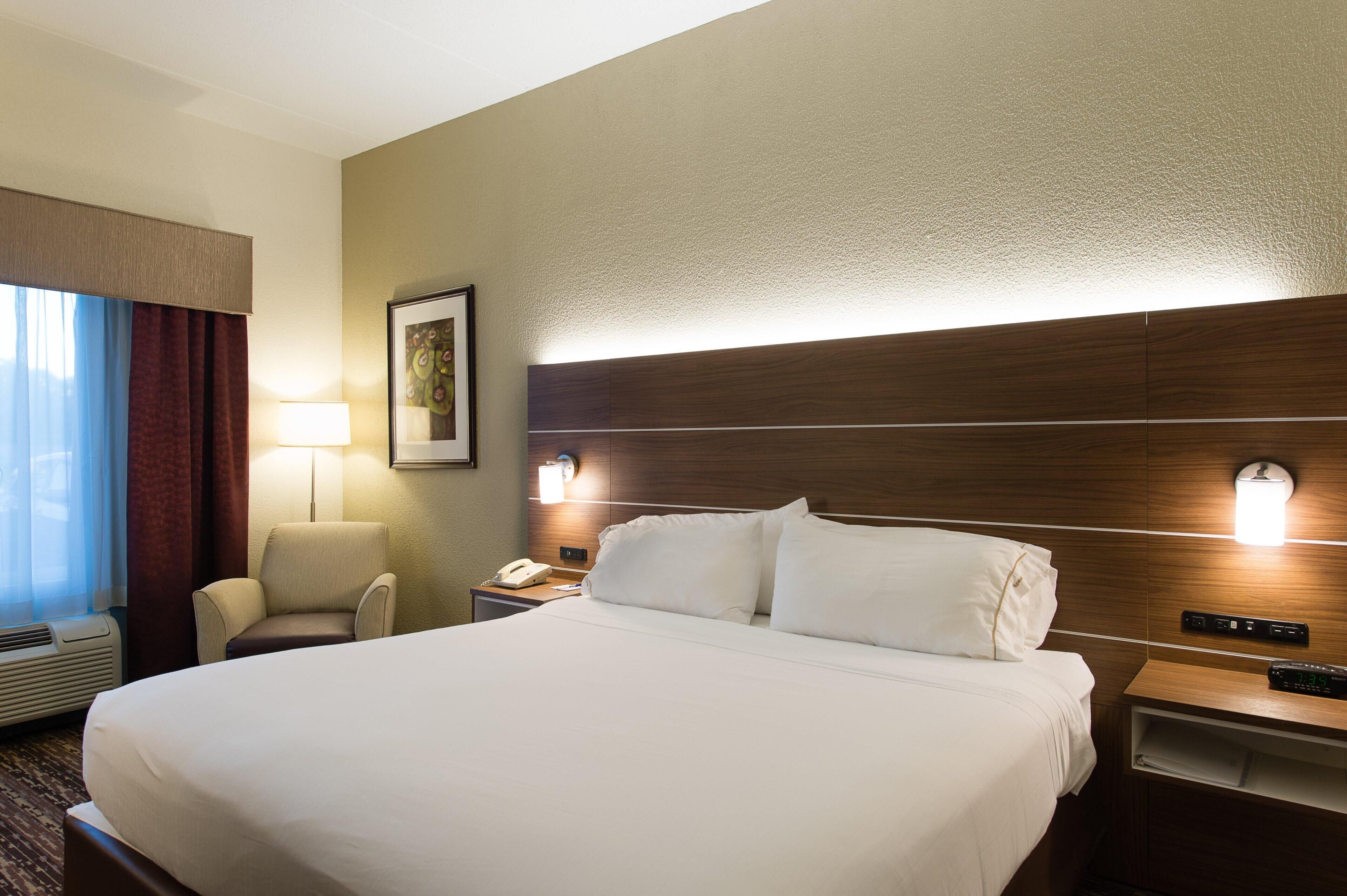 Una camera d'albergo con un letto grande, una sedia, una scrivania con una lampada e una luce a parete.