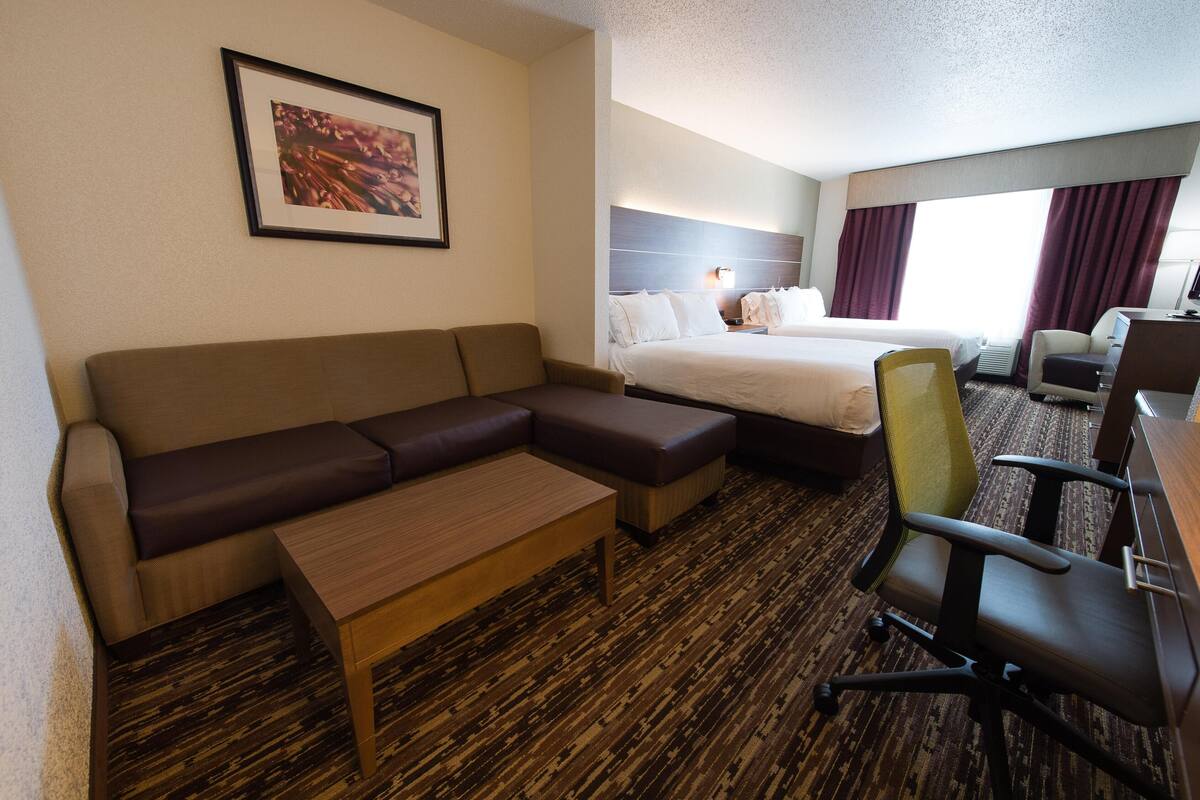 A hotel room with a sofa, a small table, a desk, a chair, a bed, and a framed picture on the wall.