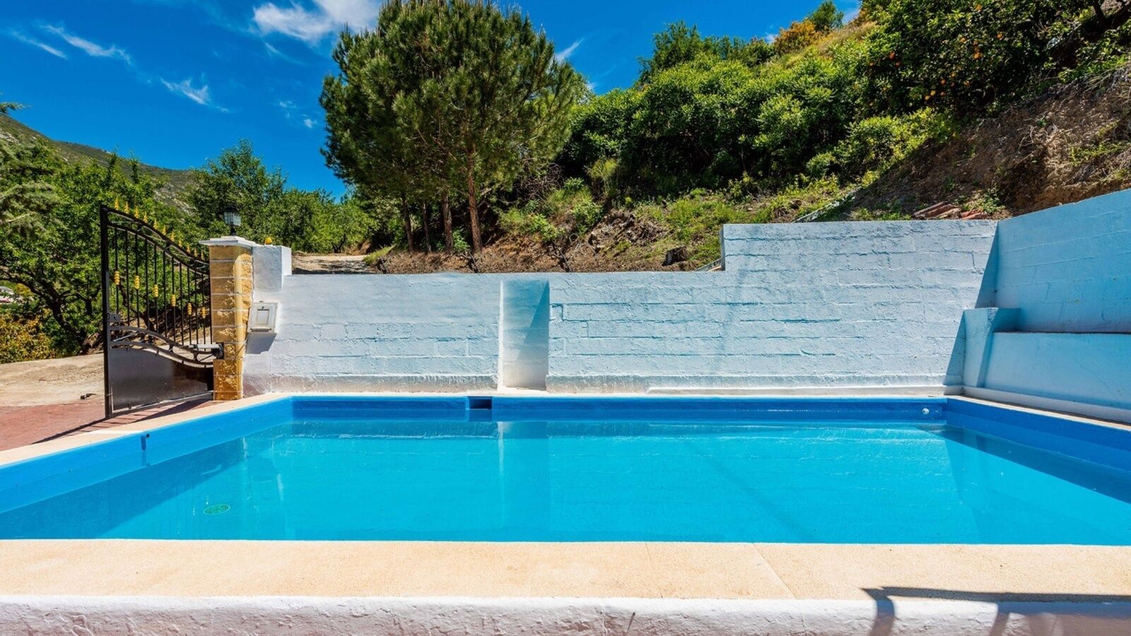 A swimming pool with a stone wall and a metal gate.