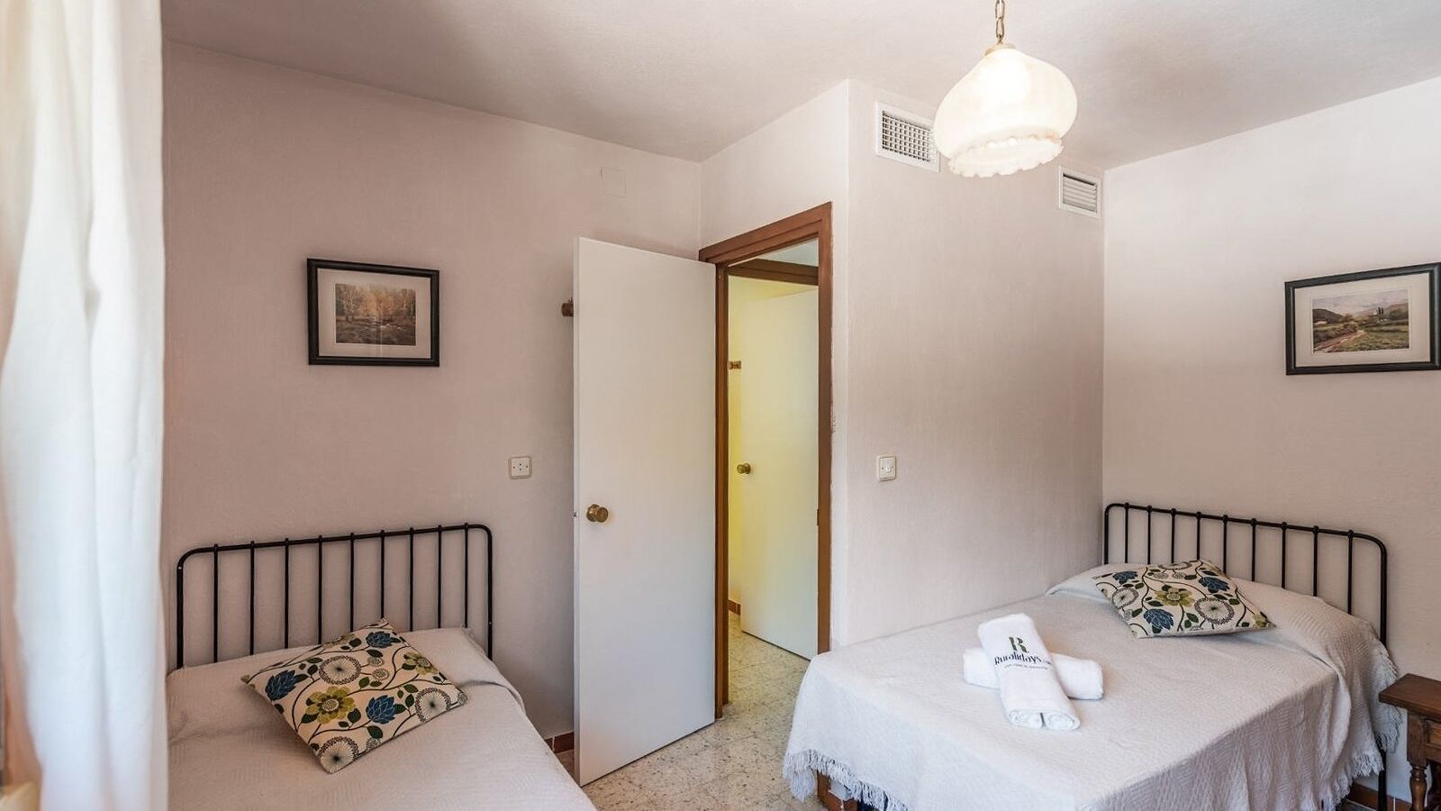 Ein Schlafzimmer mit zwei Betten, einer Tür zu einem anderen Raum und einer Deckenleuchte.