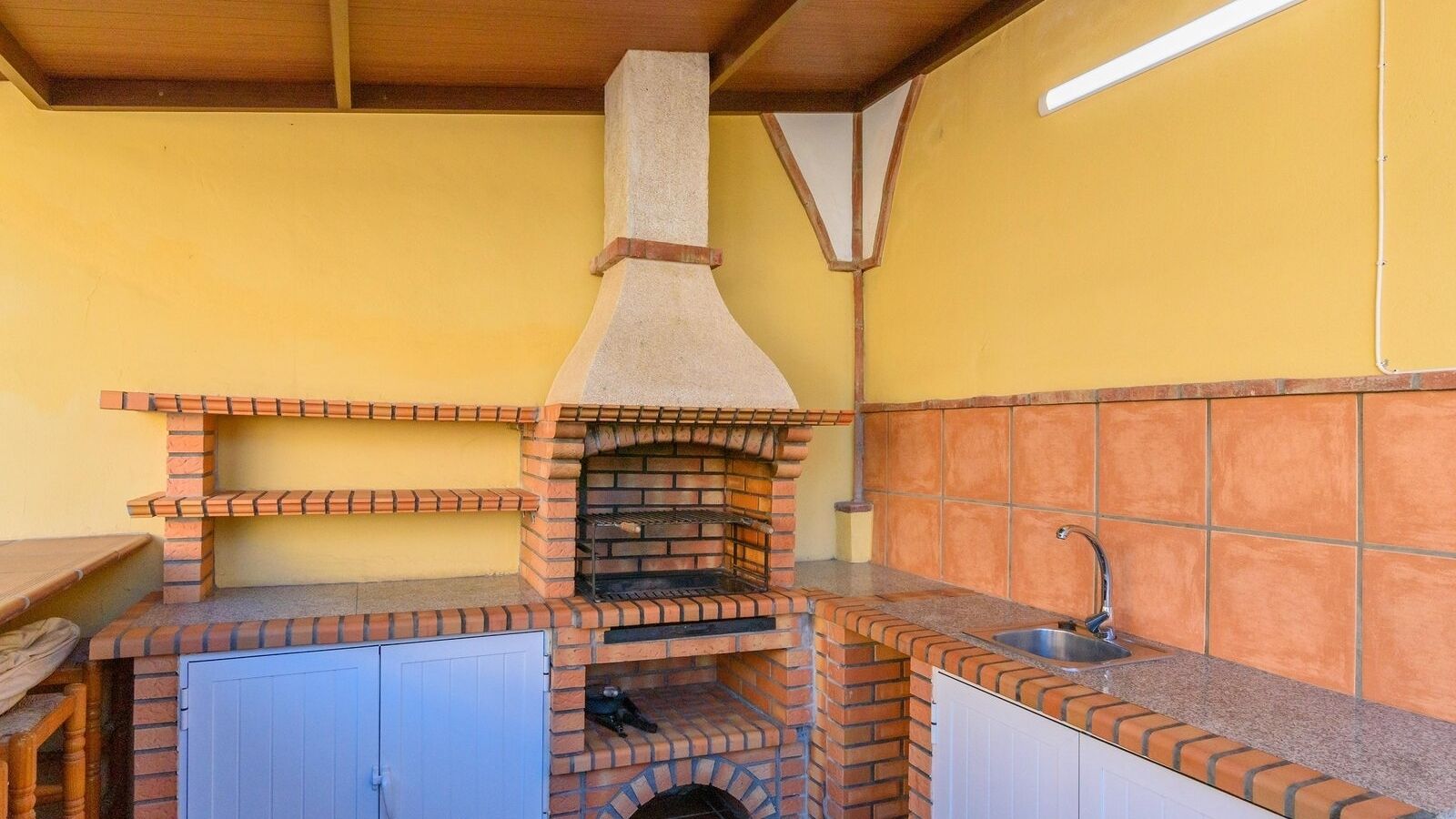 Cucina esterna con forno a mattoni, lavello e tavolo di legno.