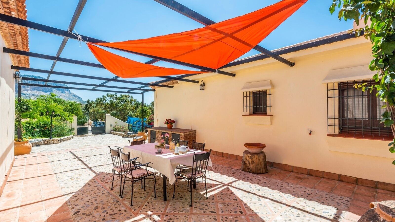 A covered patio with a table set for dining, surrounded by chairs, and a decorative bowl on a tree stump.