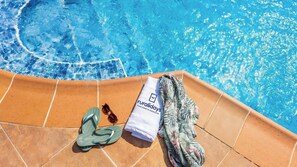 Un espace aménagé au bord de la piscine avec une serviette, des tongs et des lunettes de soleil.