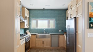Una cocina compacta con armarios de madera, un refrigerador de acero inoxidable y un ventanal sobre el lavamanos.