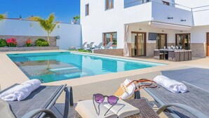 Un área de piscina moderna con sillones de descanso, un libro, gafas de sol y toallas.