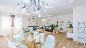 Una sala de estar moderna con una mesa de comedor de vidrio, un sofá gris y una estantería blanca.