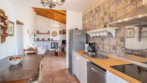 Une cuisine avec une table en bois, un réfrigérateur, une machine à café et un plan de travail carrelé.