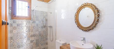 Een badkamer met douche, toilet, wastafel en een decoratieve spiegel.