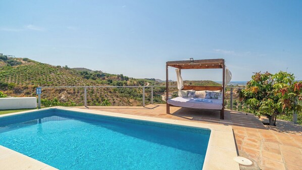 A pool with a wooden bed structure and a view of hills.