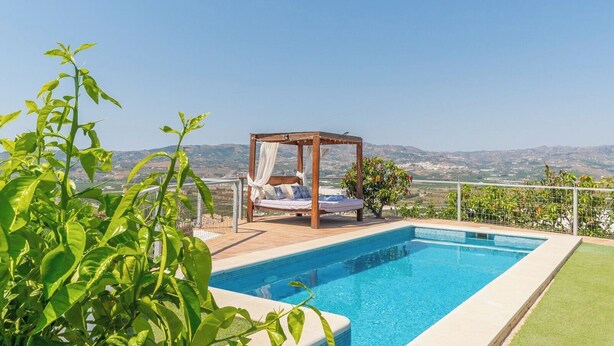 Une piscine entourée d’une terrasse en bois, un lit à baldaquin et une vue sur les collines lointaines.
