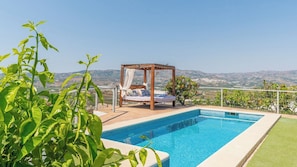 A pool with a wooden deck, a canopy bed, and a view of distant hills.