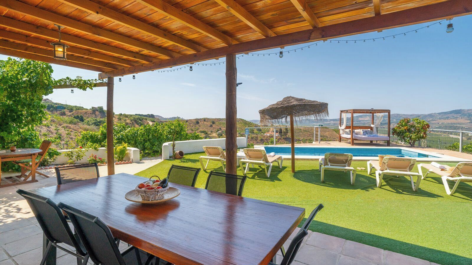 A covered patio with a pool, outdoor seating, and a view of the landscape.