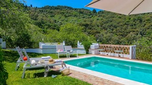 A swimming pool with lounge chairs and umbrellas, surrounded by lush greenery and hills. - Casa Piedras de Gaucín by Ruralidays (Málaga)