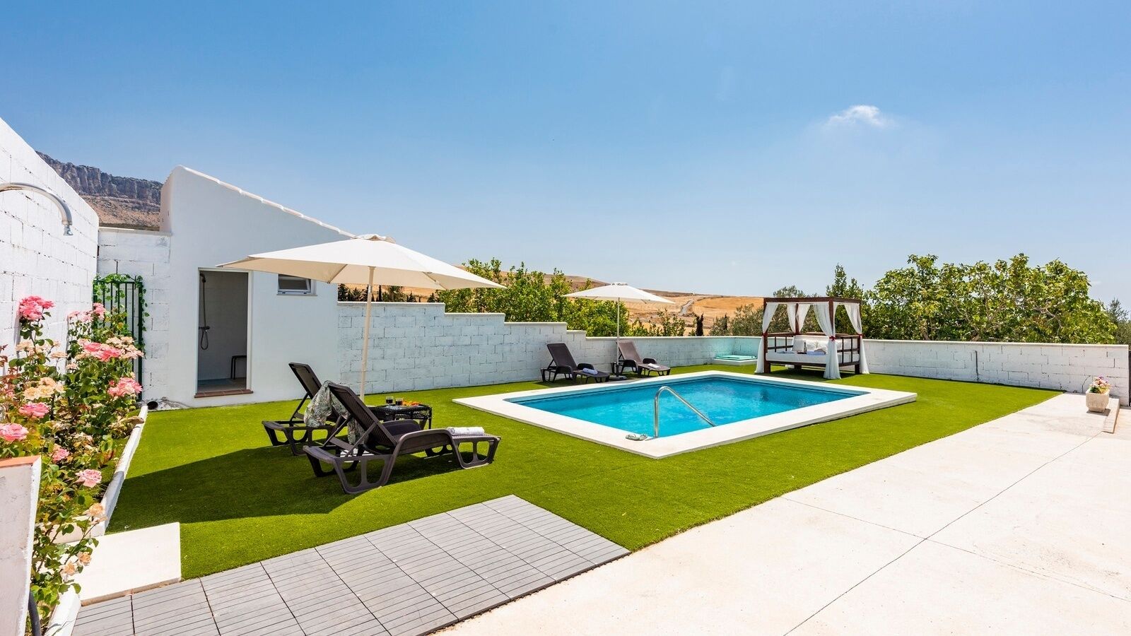 A backyard with a swimming pool, a pergola, and a white building with a door.
