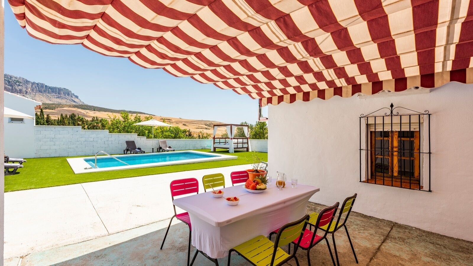 Un patio con piscina, una mesa y sillas, y un toldo a rayas.