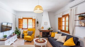 A living room with a fireplace, a sofa, a yellow armchair, and a television. - El Llano del Torcal Antequera - La Higuera by Ruralidays (Málaga)
