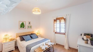 A well-lit bedroom with a wooden bed, bedside lamps, a window with curtains, and a small table with a plant and a candle. - El Llano del Torcal Antequera - La Higuera by Ruralidays (Málaga)