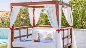 A wooden canopy bed with white bedding and red ribbons, positioned near a pool with a view of greenery. - El Llano del Torcal Antequera - La Higuera by Ruralidays (Málaga)