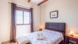 A bedroom with a bed, two bedside lamps, a window with curtains, a framed picture on the wall, and a bedside table. - Villa Eugenia Torrox by Ruralidays (Málaga)