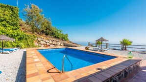 A rectangular pool with a metal ladder, surrounded by pebble beach and a stone wall. - Villa Eugenia Torrox by Ruralidays (Málaga)