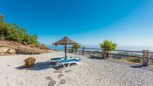 A pebble beach with lounge chairs and a thatched umbrella, overlooking a coastal view. - Villa Eugenia Torrox by Ruralidays (Málaga)