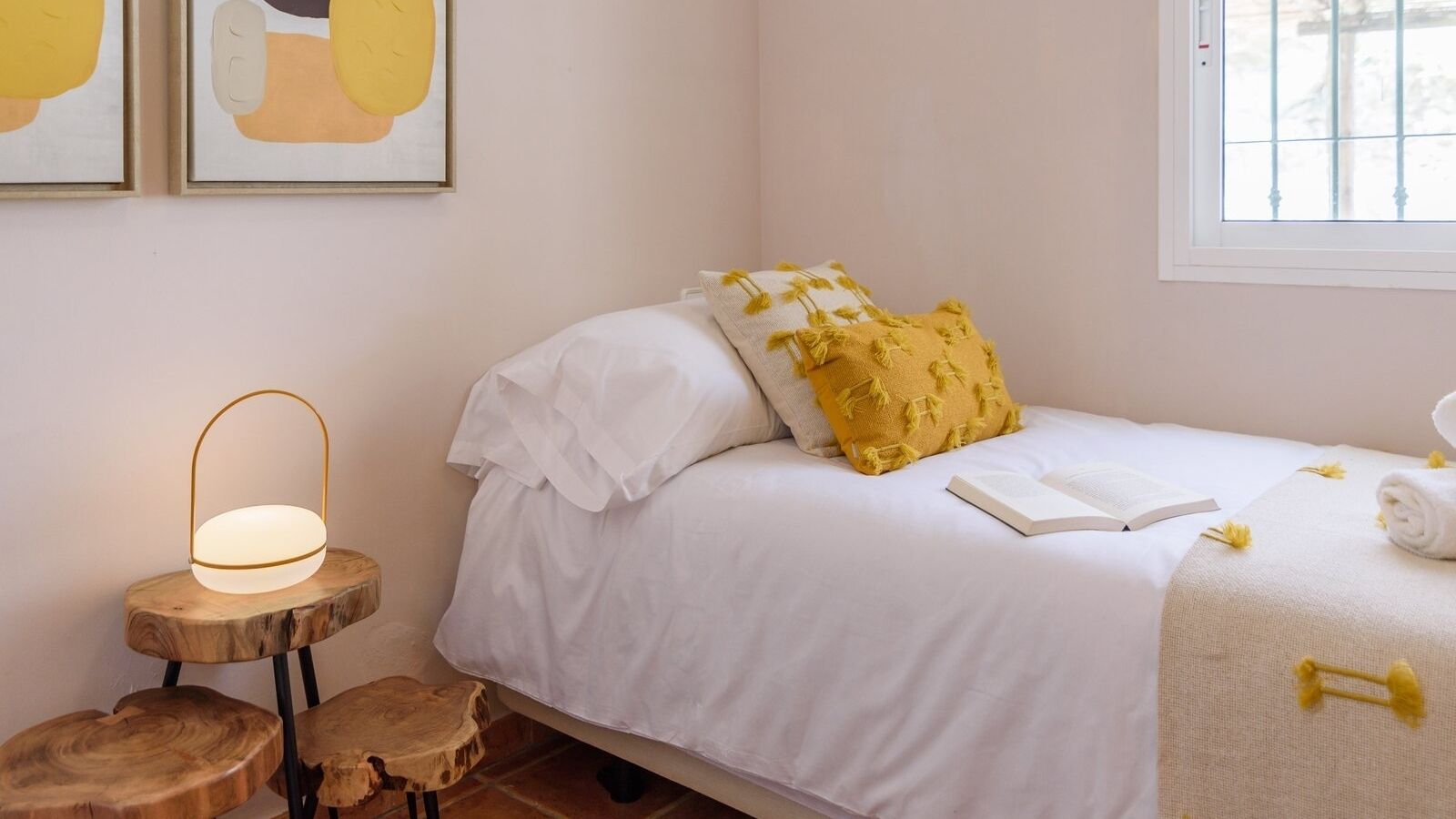 Een slaapkamer met een bed, een nachtkastje met een lamp en een raam.