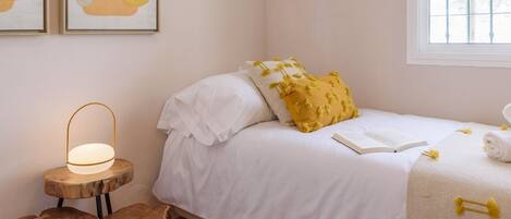 Een slaapkamer met een bed, een nachtkastje met een lamp en een raam.