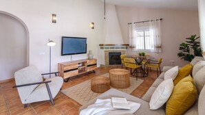 A living room with a TV, sofa, chairs, a fireplace, and a dining area. - Cortijo Baeza Torrox by Ruralidays (Málaga)