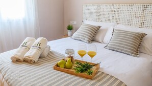 A neatly made bed with striped bedding, two rolled towels, a tray with pears, glasses of orange juice, and a small potted plant. - Cortijo Baeza Torrox by Ruralidays (Málaga)