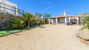 A spacious outdoor area with a gravel ground, a stone wall, and a white building with a tiled roof. - Casa Aranda Villanueva de la Concepción by Ruralidays (Málaga)