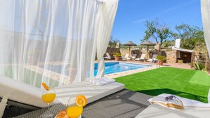 A poolside area with a bed, a glass of orange juice, and a pair of sunglasses on the bed. - Casa Aranda Villanueva de la Concepción by Ruralidays (Málaga)