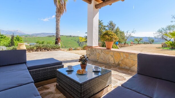 An outdoor seating area with wicker furniture and a glass table, overlooking a scenic landscape. - Casa Aranda Villanueva de la Concepción by Ruralidays (Málaga)