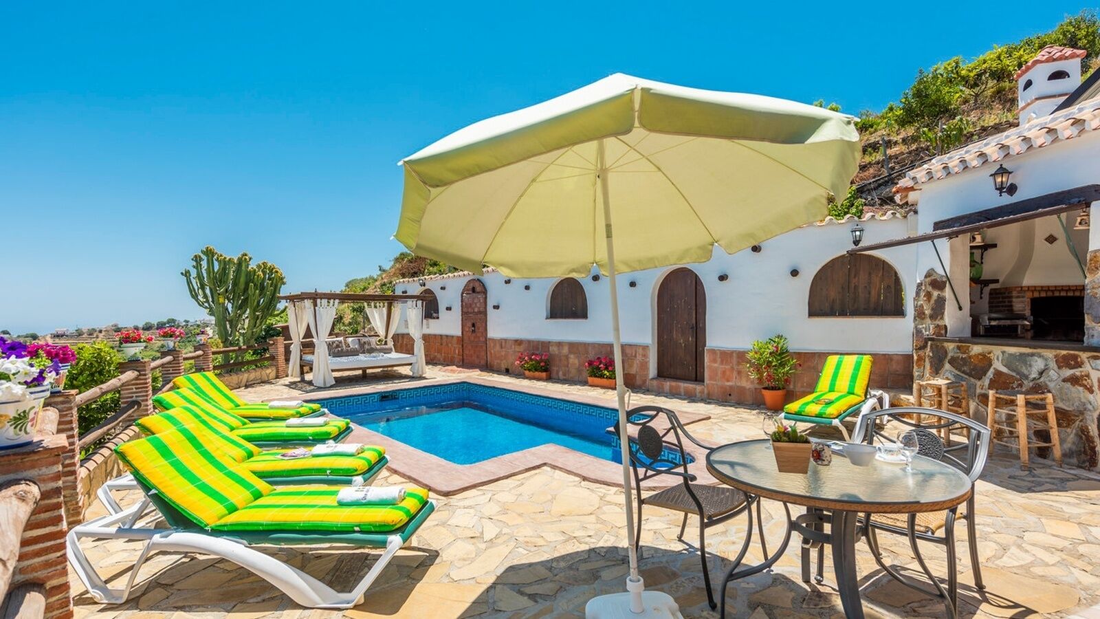 A pool area with lounge chairs, a table, and a pergola with an umbrella.