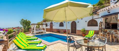 A pool area with lounge chairs, a table, and a pergola with an umbrella.