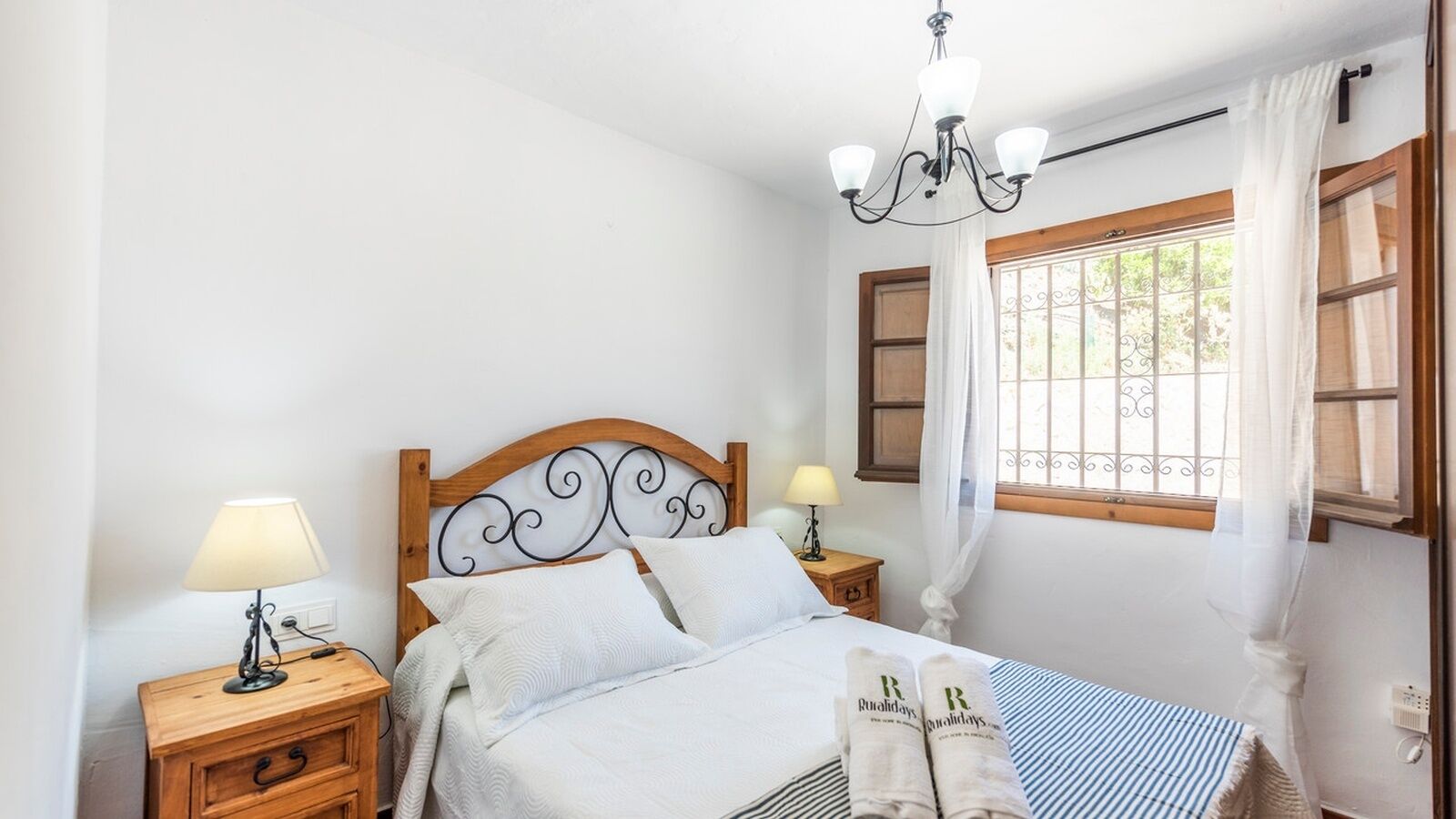 A neatly made bed with white linens, a wooden headboard, two bedside tables with lamps, and a window with curtains.