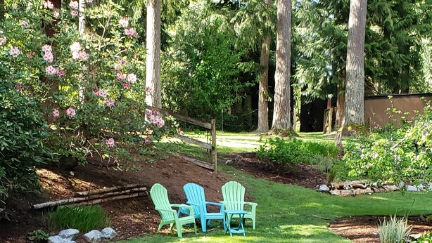Un jardín con terraza de madera, dos sillas Adirondack verdes y un pequeño estanque.