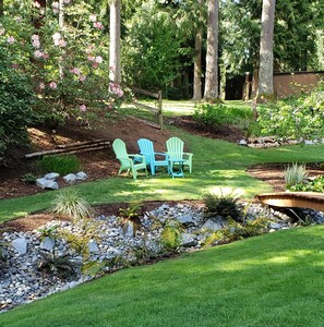 A garden with a wooden deck, two green Adirondack chairs, and a small pond.
