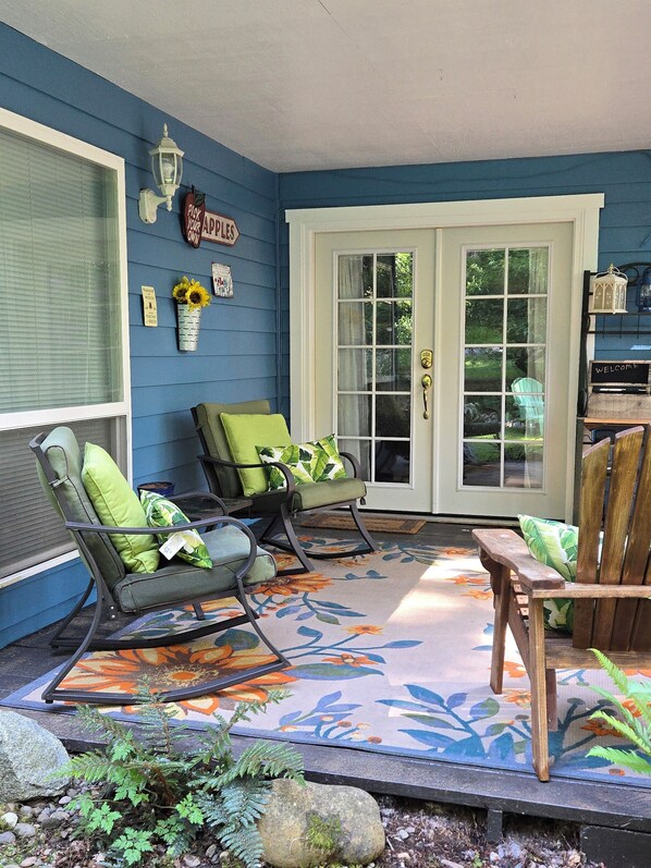 A porch with rocking chairs, a wooden table, and a door with glass panels.