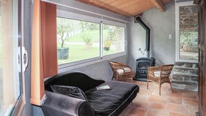 A cozy room with a black sofa, two wicker chairs, a stone wall, and a wood-burning stove. - Nice home in Thueyts with WiFi (Thueyts)