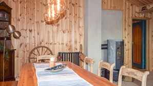 A wooden dining room with a long table, chairs, a vintage lamp, and a wood-burning stove.