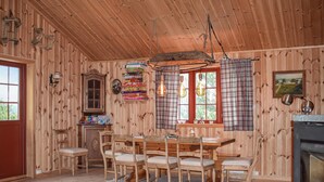 A wooden cabin interior with a dining table and chairs, a fireplace, and plaid curtains.